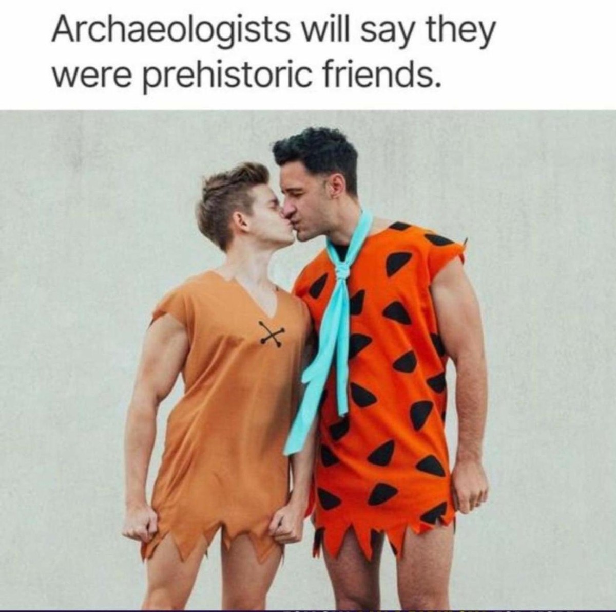 Two men dressed up as Fred Flintstone and his buddy Barney from the Flintstones, kissing in unmistakeably very gay way, with the text above the pic saying 'Archaeologists will say they were prehistoric friends'